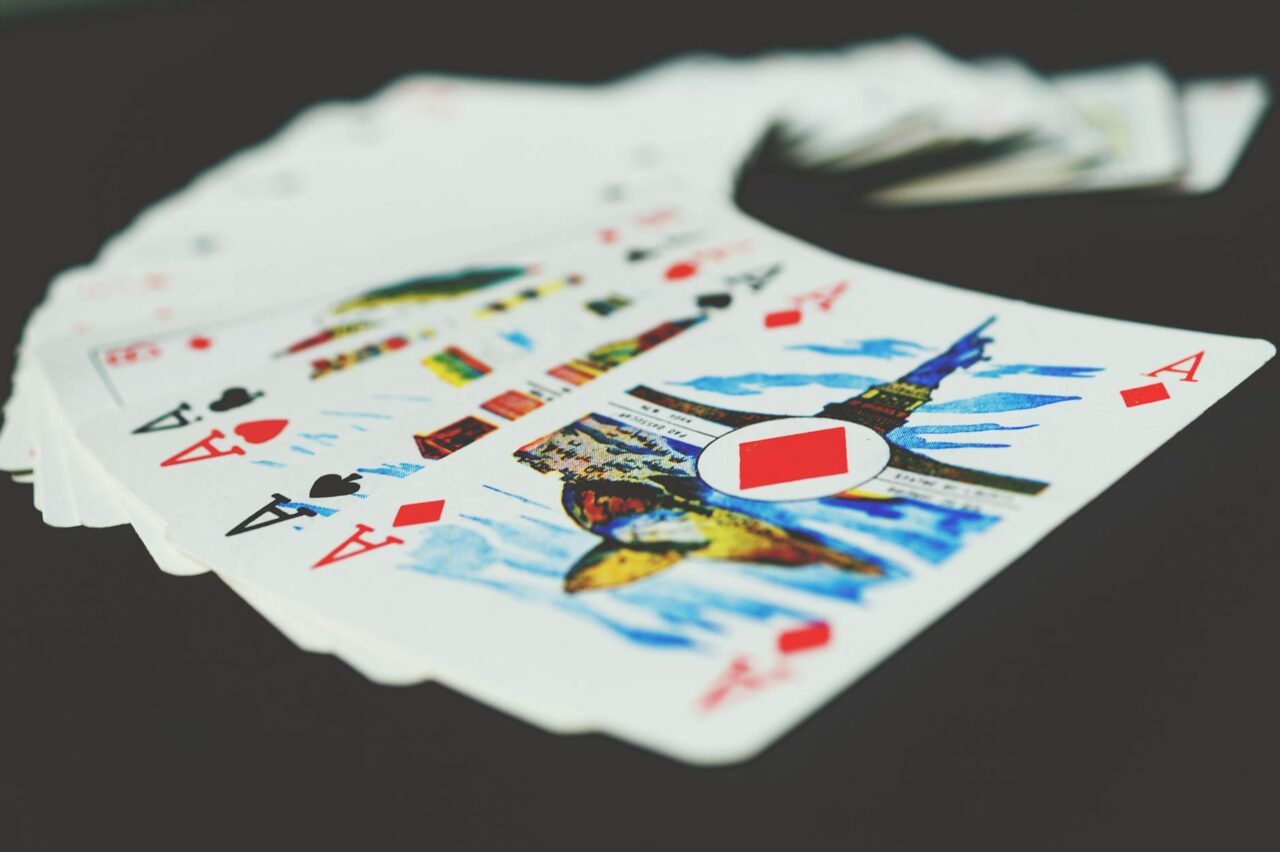 poker-casino-HT Pachet de cărți de joc răsfirat în evantai pe o suprafață neagră, cu așii vizibili